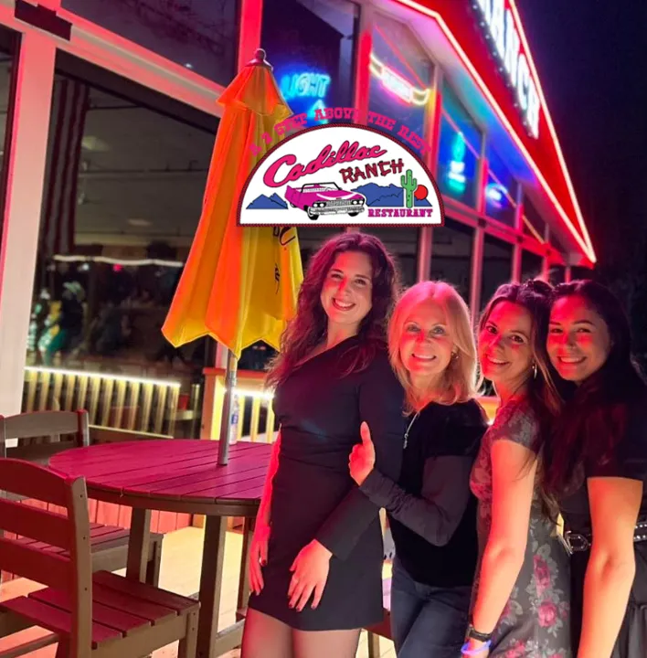 Friends posing together under the lit Cadillac Ranch sign at night